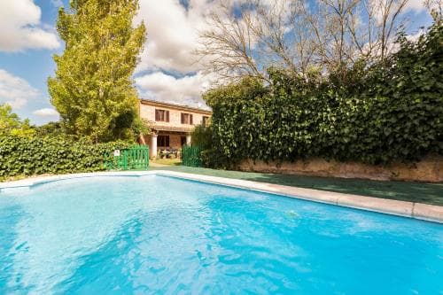 A serene private villa with a crystal-clear pool surrounded by lush greenery under a partly cloudy sky, ideal for a tranquil vacation getaway.