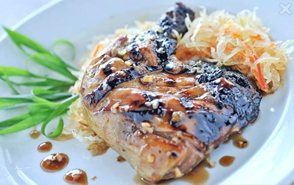 A beautifully plated dish featuring glazed meat garnished with shredded vegetables and green onions on a white plate, ideal for culinary enthusiasts exploring international cuisine options.