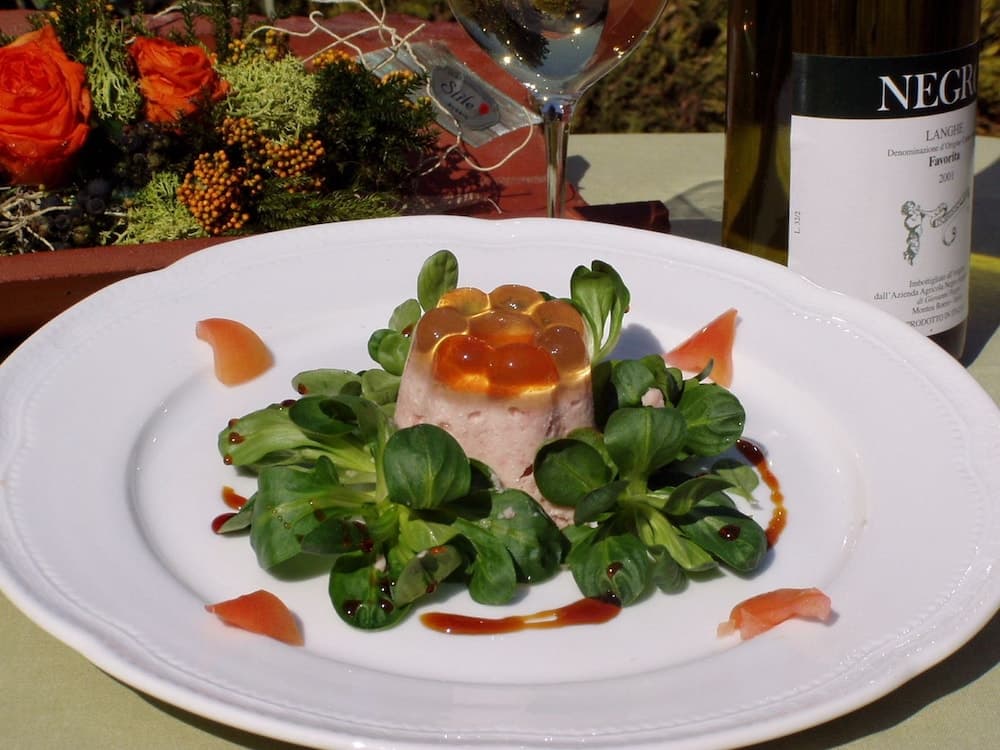 A beautifully plated gourmet dish with fresh greens and a savory centerpiece is elegantly set on an outdoor table, complemented by a bottle of Negro wine and vibrant floral arrangements, perfect for a romantic dining experience or culinary photography.