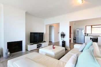 A cozy, modern living room with white furniture, a fireplace, and an open kitchen in the background creates a serene atmosphere ideal for a relaxing vacation rental experience.