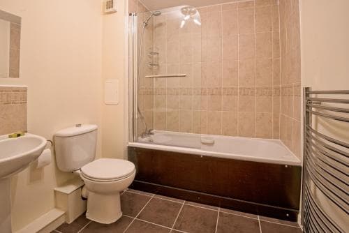 A cozy hotel bathroom features a tiled shower-over-bath setup, white fixtures including a toilet and sink, and a modern towel radiator, ideal for travelers seeking comfort and functionality.