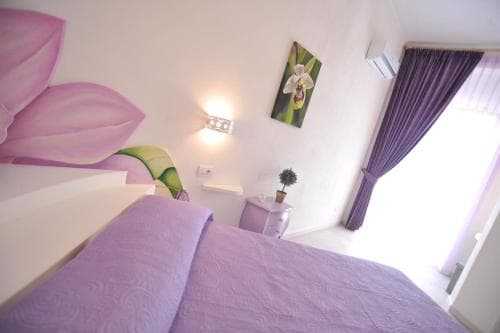 A cozy bedroom with lavender-themed decor, featuring a neatly made bed, floral artwork, and soft lighting, creates a serene atmosphere ideal for travelers seeking relaxation.