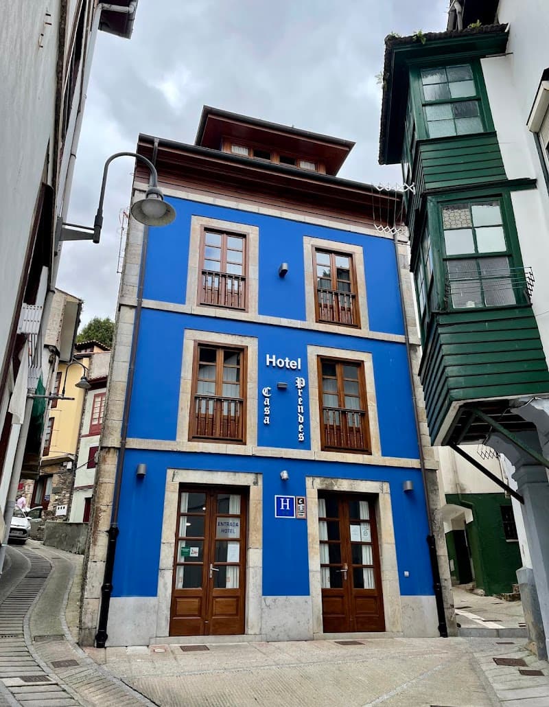 A charming blue-painted hotel with wooden balconies stands invitingly on a quaint street in Cudillero, Asturias, Spain, perfect for travelers seeking a cozy and picturesque stay.