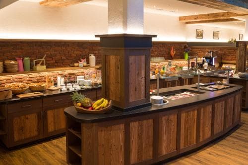 A cozy hotel buffet area features rustic wooden counters, a brick wall backdrop, fresh fruit displays, and a warm inviting atmosphere ideal for travelers seeking a comfortable dining experience.