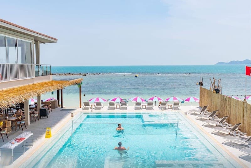 A serene beach club scene features a vibrant poolside area with lounge chairs and pink umbrellas overlooking the turquoise ocean, ideal for travelers seeking relaxation and luxury in a tropical paradise.