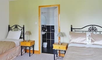 A cozy hotel room features two neatly made beds with beige linens, wooden nightstands with lamps, and an open doorway leading to a bathroom, ideal for travelers seeking comfort and convenience.