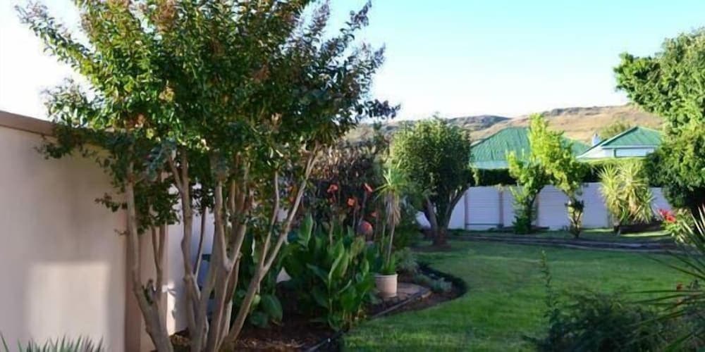 A serene suburban garden with lush greenery, vibrant plants, and a distant hillside offers a tranquil retreat, ideal for travelers seeking peaceful accommodation in a residential area.