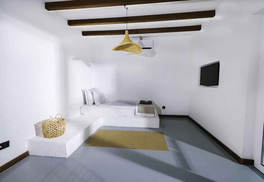 A serene minimalist bedroom with white walls, wooden beams, a cozy daybed, and a woven basket creates a tranquil retreat ideal for relaxation and mindfulness practices.
