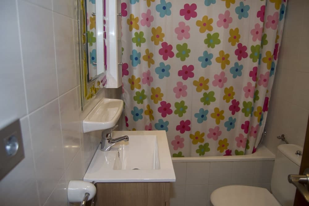A cozy bathroom features a vibrant floral shower curtain, white tiled walls, and a compact sink setup, ideal for travelers seeking a cheerful and functional space.