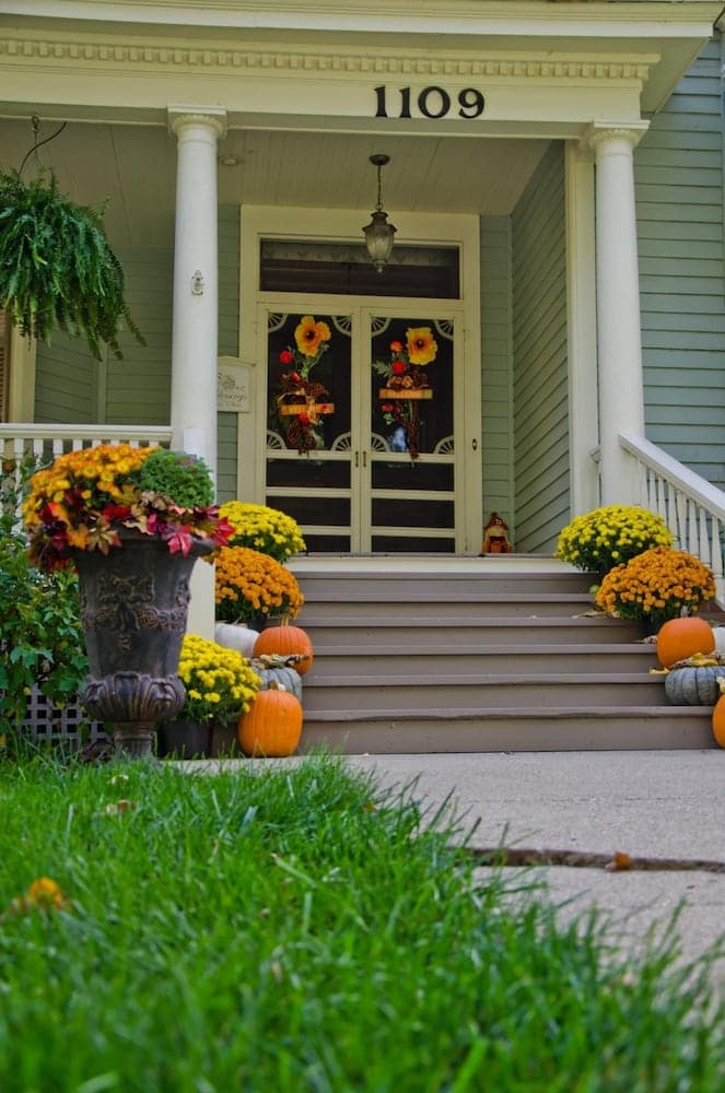 A charming residential porch adorned with autumnal decorations including vibrant mums, pumpkins, and festive wreaths creates a welcoming seasonal atmosphere ideal for fall-themed travel photography.