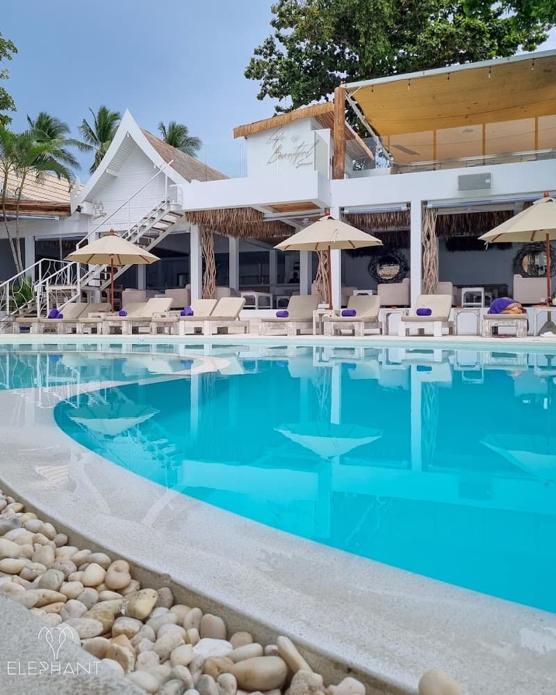 A serene tropical resort scene featuring a crystal-clear pool lined with lounge chairs and umbrellas, set against a backdrop of lush palm trees and modern beachside architecture, ideal for travelers seeking relaxation and luxury in Koh Samui, Thailand.