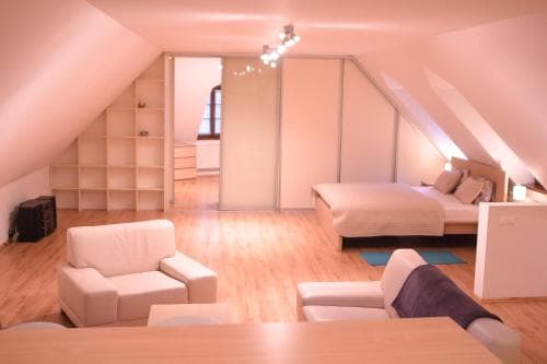 A cozy attic apartment features a warm, inviting bedroom with a neatly made bed, modern furniture, wooden flooring, and soft lighting, ideal for travelers seeking a comfortable and stylish retreat.