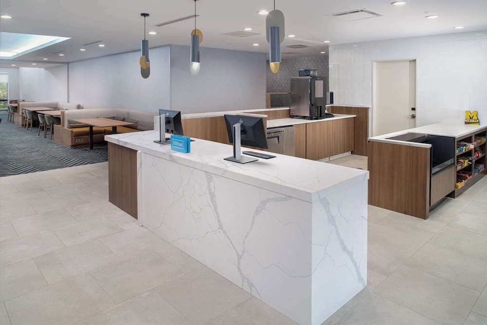 A modern hotel lobby features sleek marble counters, contemporary lighting, and comfortable seating areas, creating an inviting atmosphere ideal for travelers seeking a professional yet cozy check-in experience.