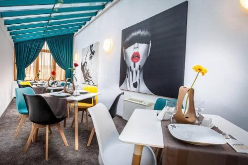A stylish indoor dining area features modern art on white walls, vibrant teal accents, and neatly set tables, creating an inviting atmosphere perfect for travelers seeking a chic restaurant experience.