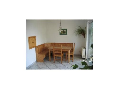 A cozy indoor dining nook with wooden furniture, tiled flooring, and greenery near a glass door, ideal for travelers seeking a quaint and comfortable accommodation space.