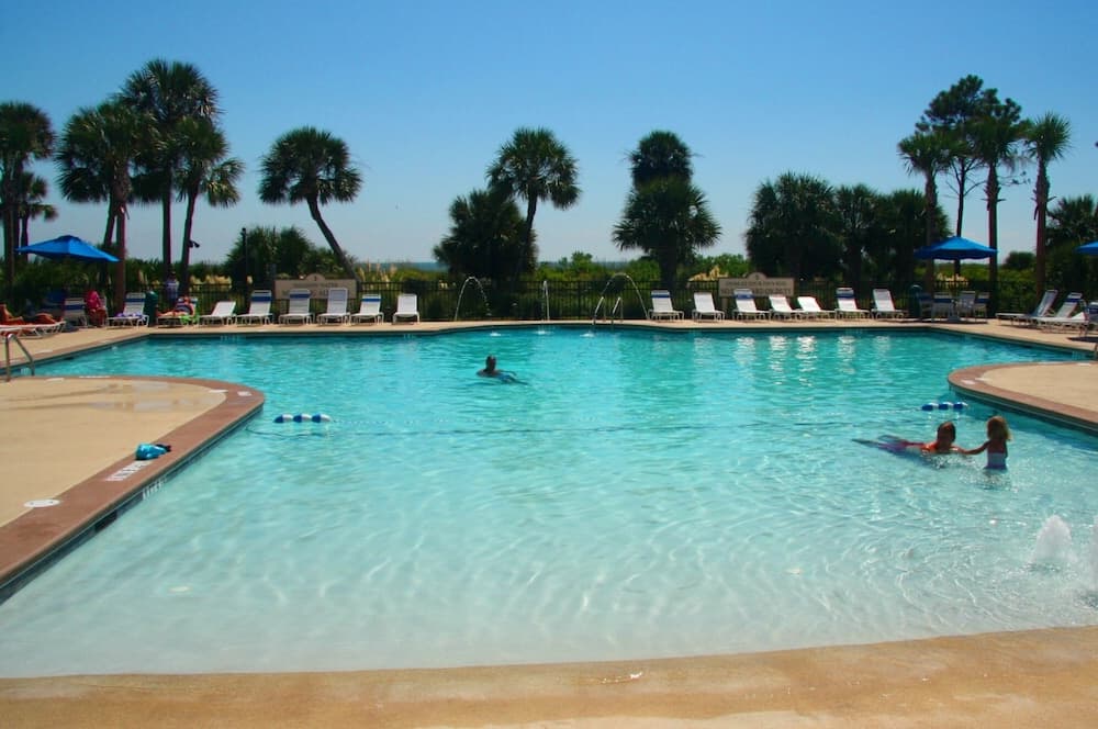 A serene resort pool surrounded by palm trees offers a relaxing tropical getaway with lounge chairs, blue umbrellas, and clear blue water perfect for family vacations.