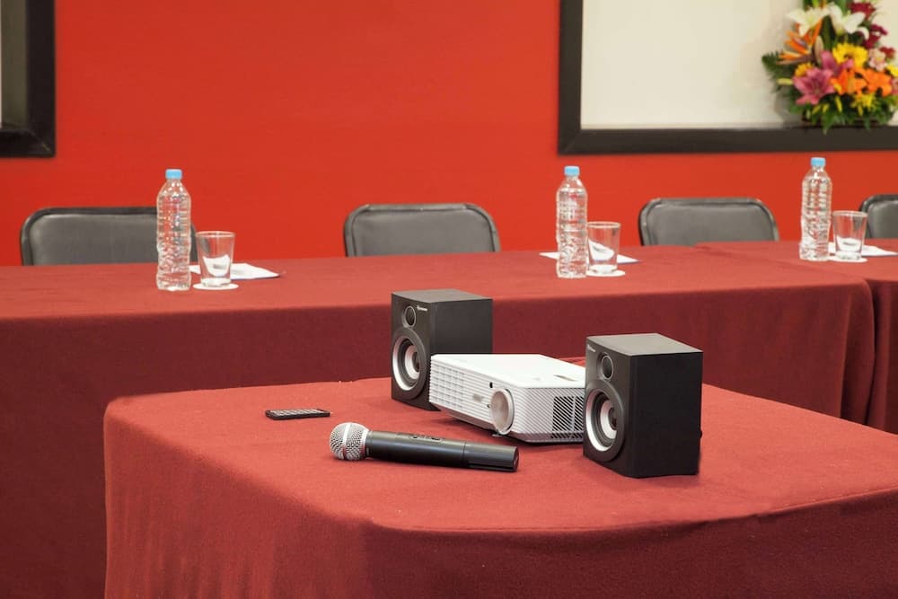 A vibrant conference room setup features red draped tables adorned with water bottles, glasses, a projector, speakers, and a microphone, ideal for professional presentations or meetings.