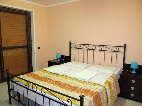 A cozy hotel room features a neatly made bed with a yellow patterned blanket, black metal frame, and matching bedside tables with blue lamps, ideal for travelers seeking comfort in a simple yet inviting space.