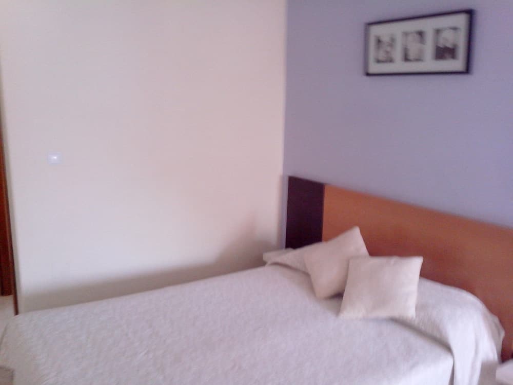 A cozy hotel room features a neatly made bed with white linens against soft-colored walls, adorned with a simple framed artwork, ideal for travelers seeking comfort and simplicity.