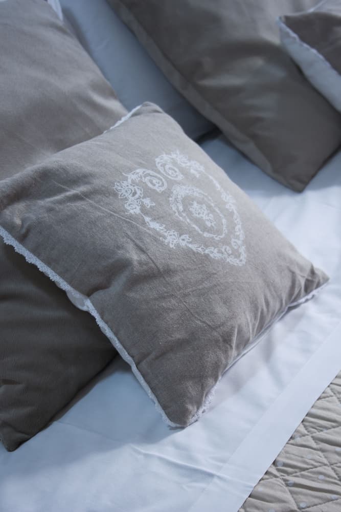A cozy bedroom scene featuring soft gray pillows with delicate white embroidery on a neatly made bed, ideal for travelers seeking comfort and relaxation in a serene lodging environment.