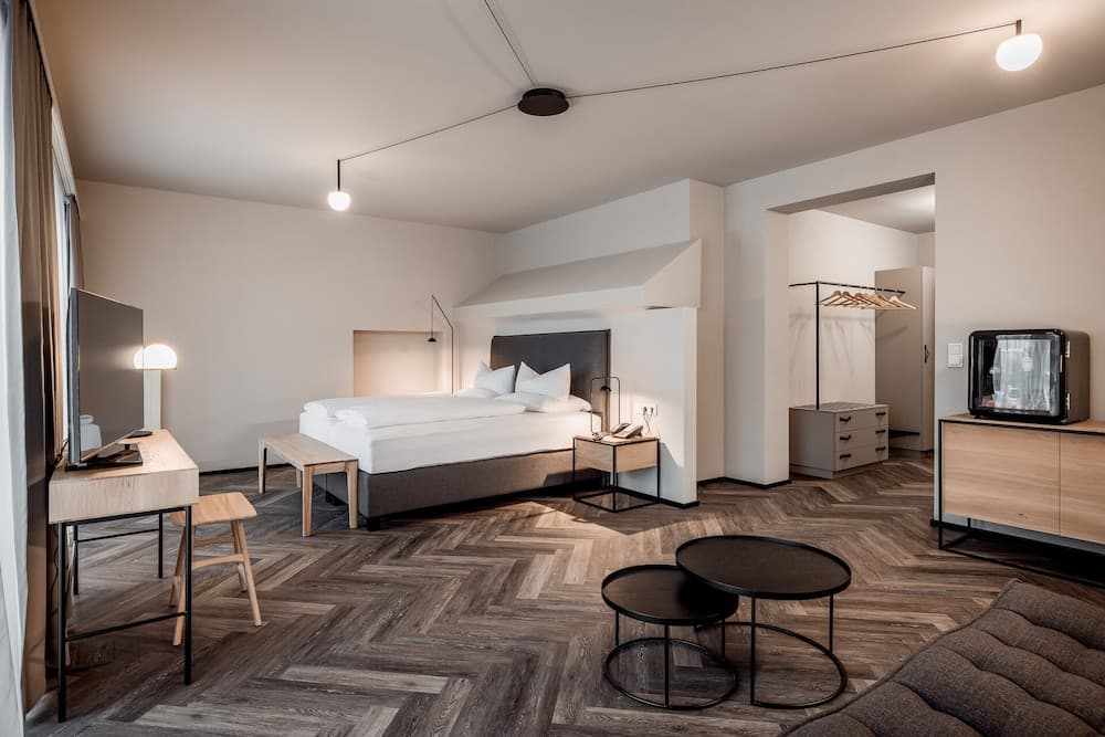 A modern hotel room features a cozy bed, sleek wooden flooring, minimalist furniture, and ambient lighting, ideal for travelers seeking comfort and style in their accommodations.