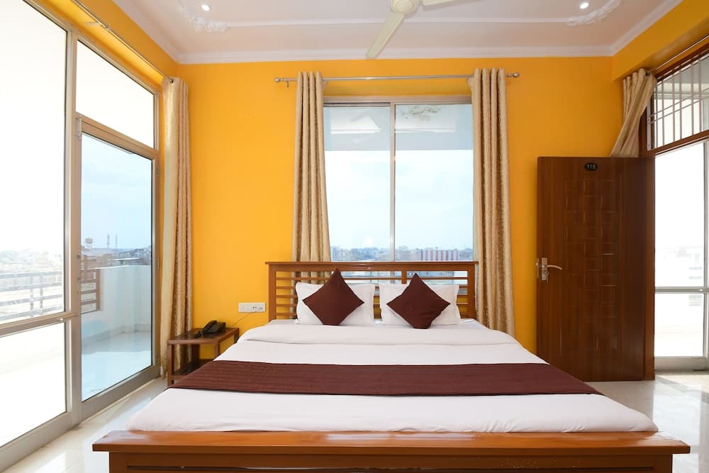 A cozy hotel room with vibrant yellow walls, a neatly made bed adorned with brown accents, large windows offering a city view, and a serene atmosphere ideal for travelers seeking relaxation.