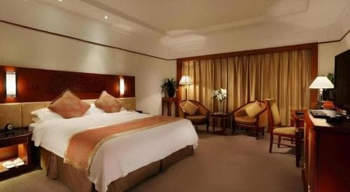 A cozy hotel room features a neatly made bed with warm-toned bedding, plush armchairs by a window with golden curtains, and ambient lighting, ideal for travelers seeking comfort and relaxation.