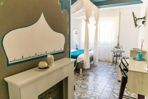 A charming, cozy bedroom with ornate tiled floors, a canopy bed draped in white fabric, and a decorative fireplace, evokes a serene and inviting atmosphere perfect for a relaxing getaway.