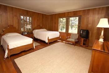A cozy cabin bedroom with wooden paneling, two neatly made beds, a vintage TV, and soft lighting creates a warm and inviting atmosphere ideal for a relaxing getaway.