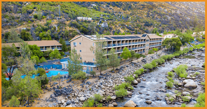 Nestled amidst lush greenery and a flowing river, the serene Yosemite View Lodge offers travelers a tranquil retreat with its cozy accommodations and inviting pool, perfect for nature enthusiasts exploring the area.