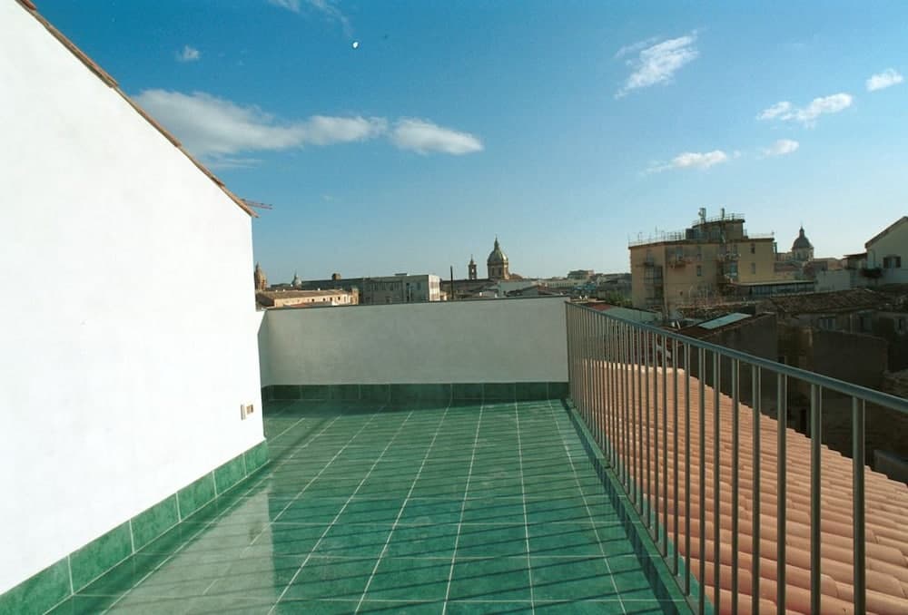 A serene rooftop terrace with green tiles overlooks a historic cityscape under a clear blue sky, ideal for travelers seeking a peaceful urban retreat.