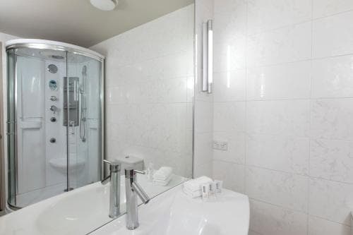 A clean, modern bathroom with white tiled walls, a glass-enclosed shower, and neatly folded towels creates a serene atmosphere ideal for travelers seeking comfort and hygiene in their accommodations.