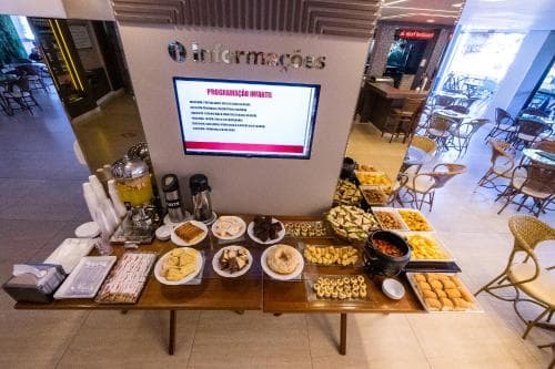 A cozy indoor café scene features a welcoming buffet table laden with assorted pastries and fruits, set against a backdrop of comfortable seating and an information kiosk, ideal for travelers seeking a relaxing breakfast spot.