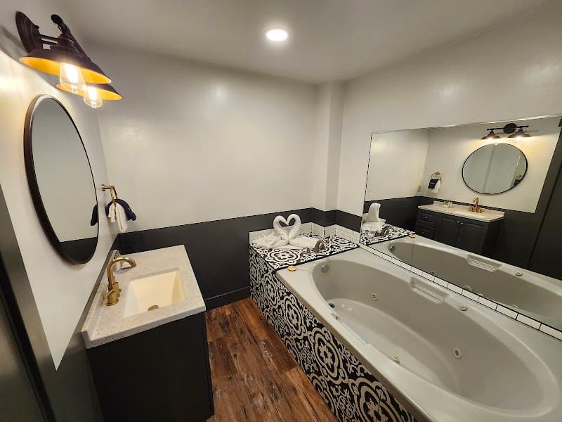 A cozy and elegant bathroom at the Heavenly Inn in South Lake Tahoe features a luxurious bathtub adorned with swan towels, modern black-and-white decor, and warm lighting, perfect for travelers seeking relaxation and comfort.