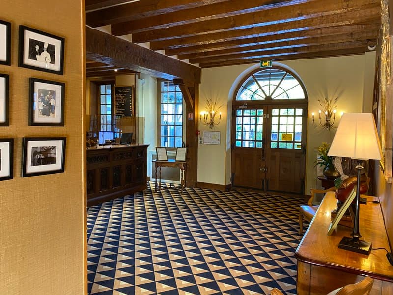 A cozy hotel lobby with wooden beams, checkered flooring, framed photos on the wall, and warm lighting creates an inviting atmosphere perfect for travelers seeking comfort and charm.