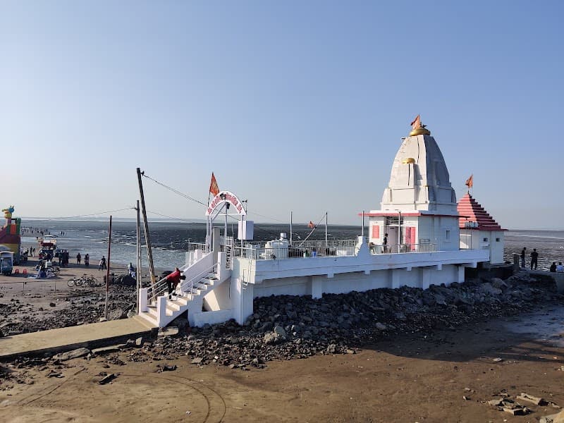 A serene coastal temple with white architecture stands on a rocky beach under a clear sky, offering travelers a tranquil spot for spiritual reflection and scenic views in Surat, Gujarat.