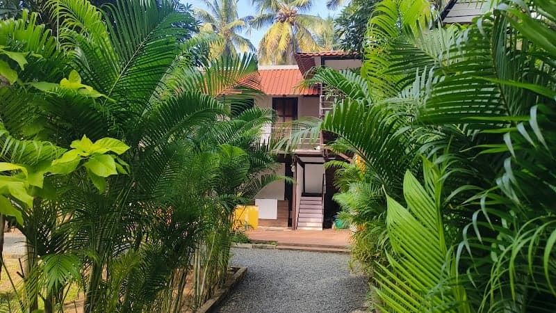 A tranquil pathway lined with lush greenery leads to a cozy two-story resort villa near Serenity Beach Road in Puducherry, ideal for travelers seeking a peaceful retreat amidst nature.