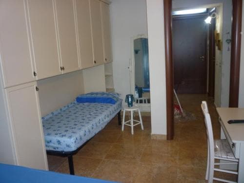 A cozy studio apartment with tiled floors, a single bed adorned with blue bedding, and a compact dining area, ideal for budget-friendly solo travelers seeking simplicity and comfort.