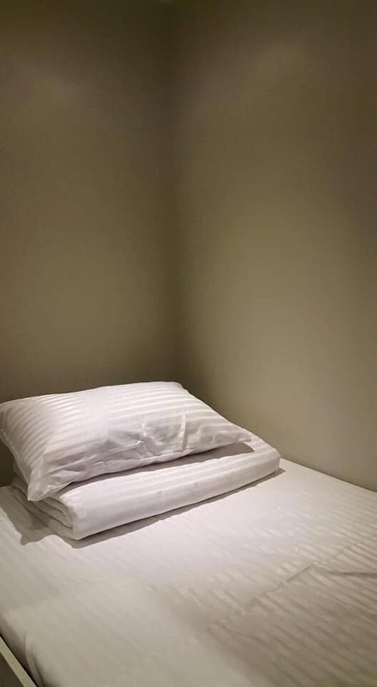 A minimalist hotel room features a neatly made bed with white striped linens in a cozy corner, ideal for travelers seeking simplicity and comfort.