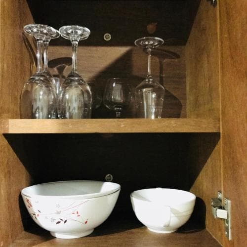 A cozy kitchen cabinet scene featuring neatly arranged wine glasses on the top shelf and elegant ceramic bowls below, ideal for showcasing home decor or culinary travel inspiration.