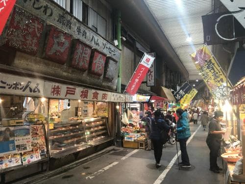 A bustling evening market scene with illuminated storefronts, colorful signs, and shoppers browsing fresh goods, capturing the lively atmosphere of a traditional Japanese marketplace ideal for cultural exploration and culinary adventures.