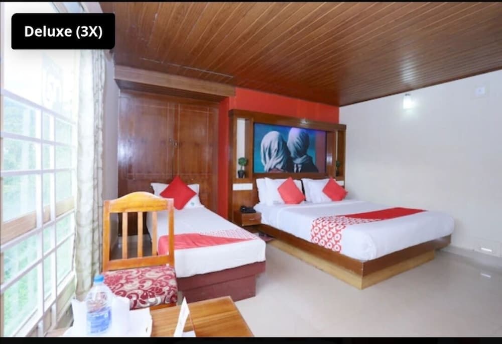 A cozy deluxe hotel room with wooden ceilings, two neatly arranged beds adorned with red accents, a vibrant wall mural, and large windows inviting natural light, ideal for travelers seeking comfort and relaxation.