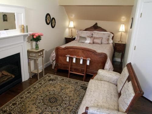 A cozy bedroom with a vintage bed, ornate rug, fireplace, and floral accents offers a charming retreat for travelers seeking a quaint and comfortable stay.