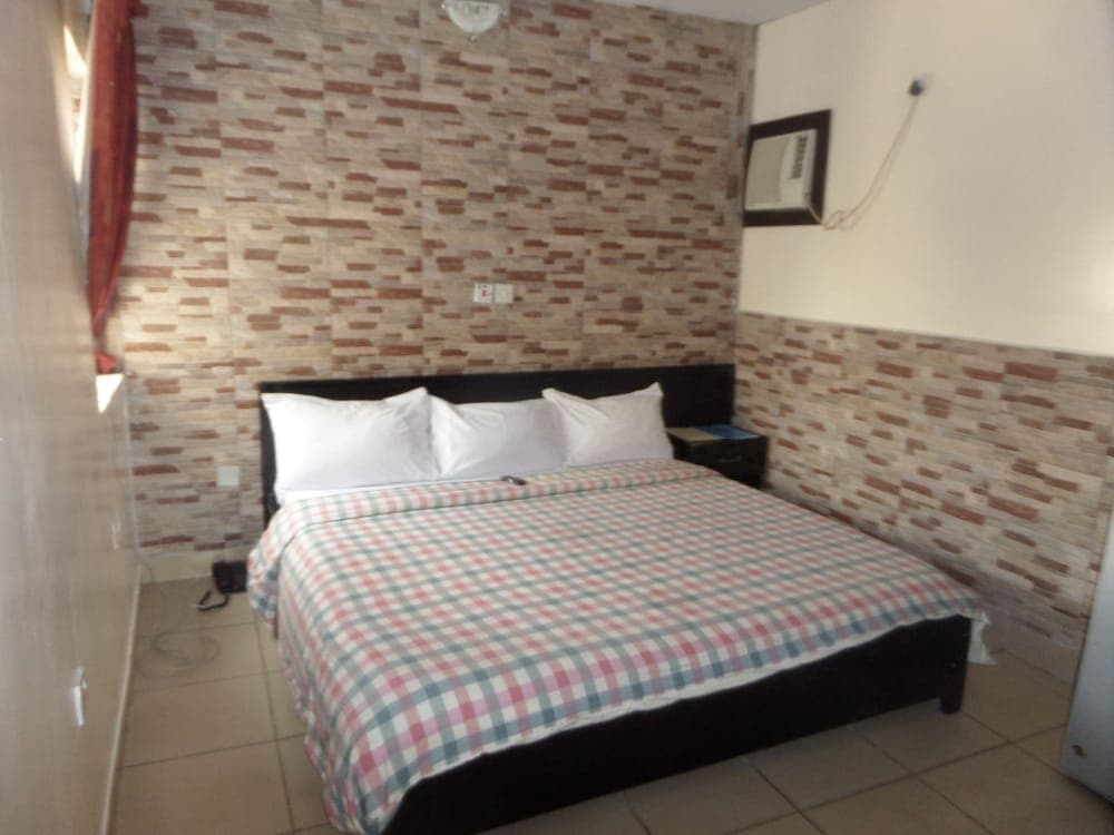 A cozy hotel room features a neatly made bed with a checkered blanket against a textured brick-patterned wall, ideal for travelers seeking comfortable accommodations.
