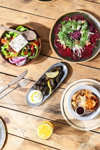 A rustic wooden table showcases vibrant Mediterranean dishes like salads, dolmas, and grilled items, creating an inviting atmosphere perfect for foodie travelers exploring local cuisine.