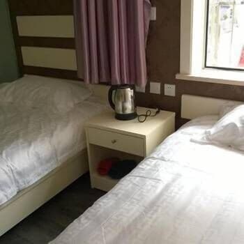 A cozy budget hotel room features two neatly made beds beside a small nightstand with a kettle, ideal for travelers seeking simple accommodations in an urban setting.