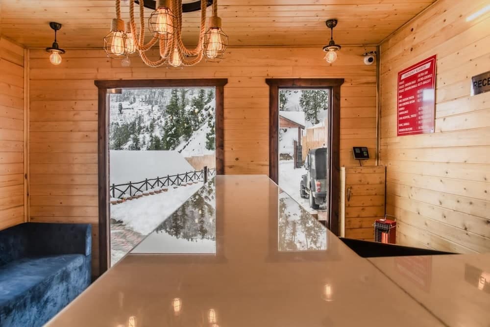 A cozy wooden cabin interior with a sleek reception desk, inviting chandelier lighting, and snowy outdoor views through open doors, perfect for a serene winter getaway.