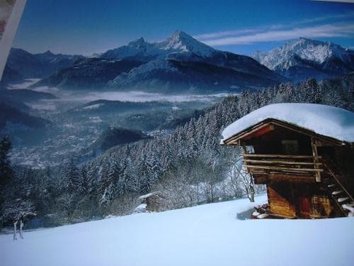 A serene winter landscape features a cozy wooden cabin nestled in snow-covered woods, overlooking a majestic mountain range, ideal for a tranquil ski retreat or nature escape.