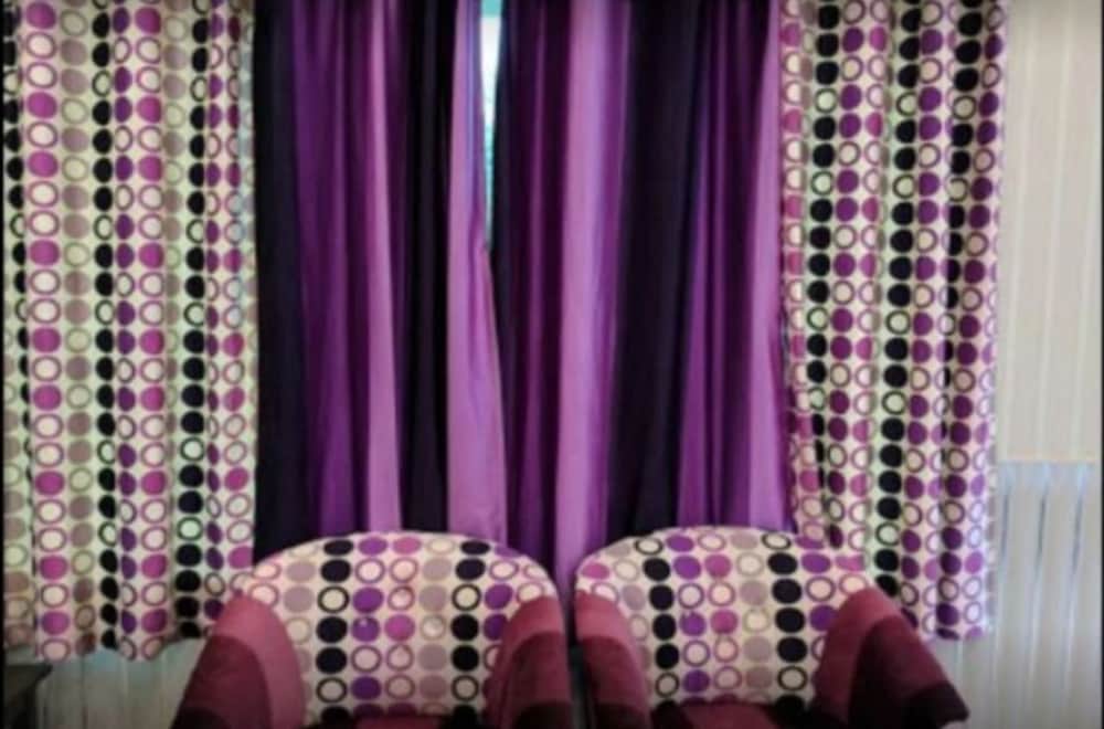 A cozy indoor seating area features vibrant purple curtains with circular patterns, complementing the matching chairs, ideal for travelers seeking a comfortable and stylish relaxation spot.