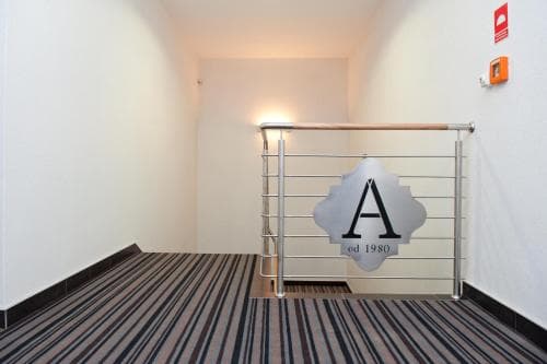 A warmly lit hotel corridor features striped carpeting, a sleek metal railing, and a minimalist design, ideal for travelers seeking modern comfort and safety amenities.